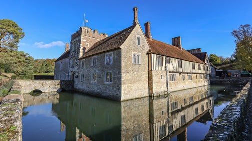 The corner of the west front of the house reflected in the moat, with a stone bridge leading to the entrance, at Ightham Mote, Kent